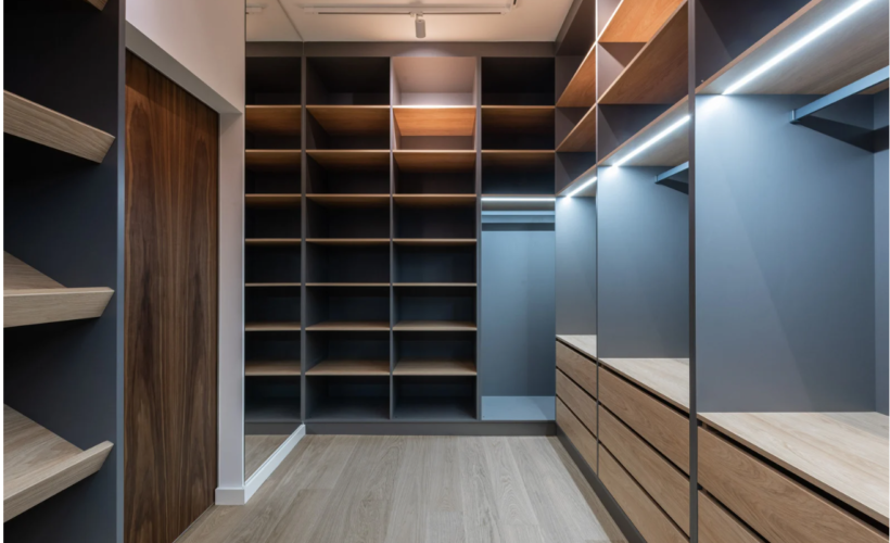 armario modular vestidor abierto de suelo a techo con estanterías, cajones y colgadores, en diferentes tonalidades de madera e iluminación interior.